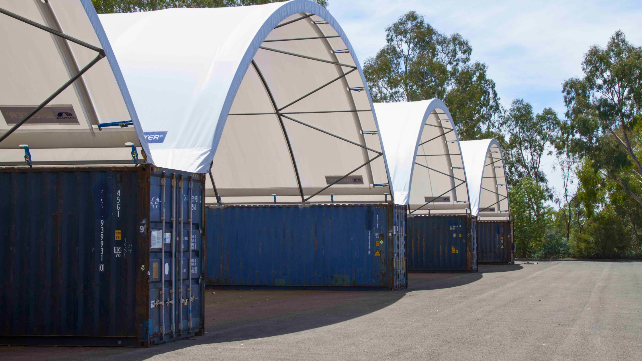 Shipping containers arranged in a row, covered by a canopy, functioning as express shelters for secure and accessible storage.